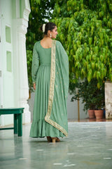 Woman in a green traditional outfit standing outdoors with greenery in the background