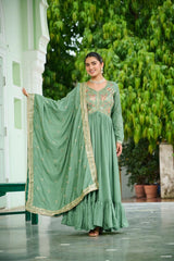 Woman in a green traditional outfit standing outdoors with greenery in the background