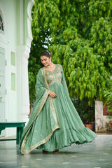 Woman in a green traditional outfit standing outdoors with greenery in the background