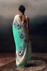 Woman wearing a teal saree with floral patterns on a dark background