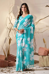 Woman wearing a turquoise saree with white floral patterns against a neutral background.