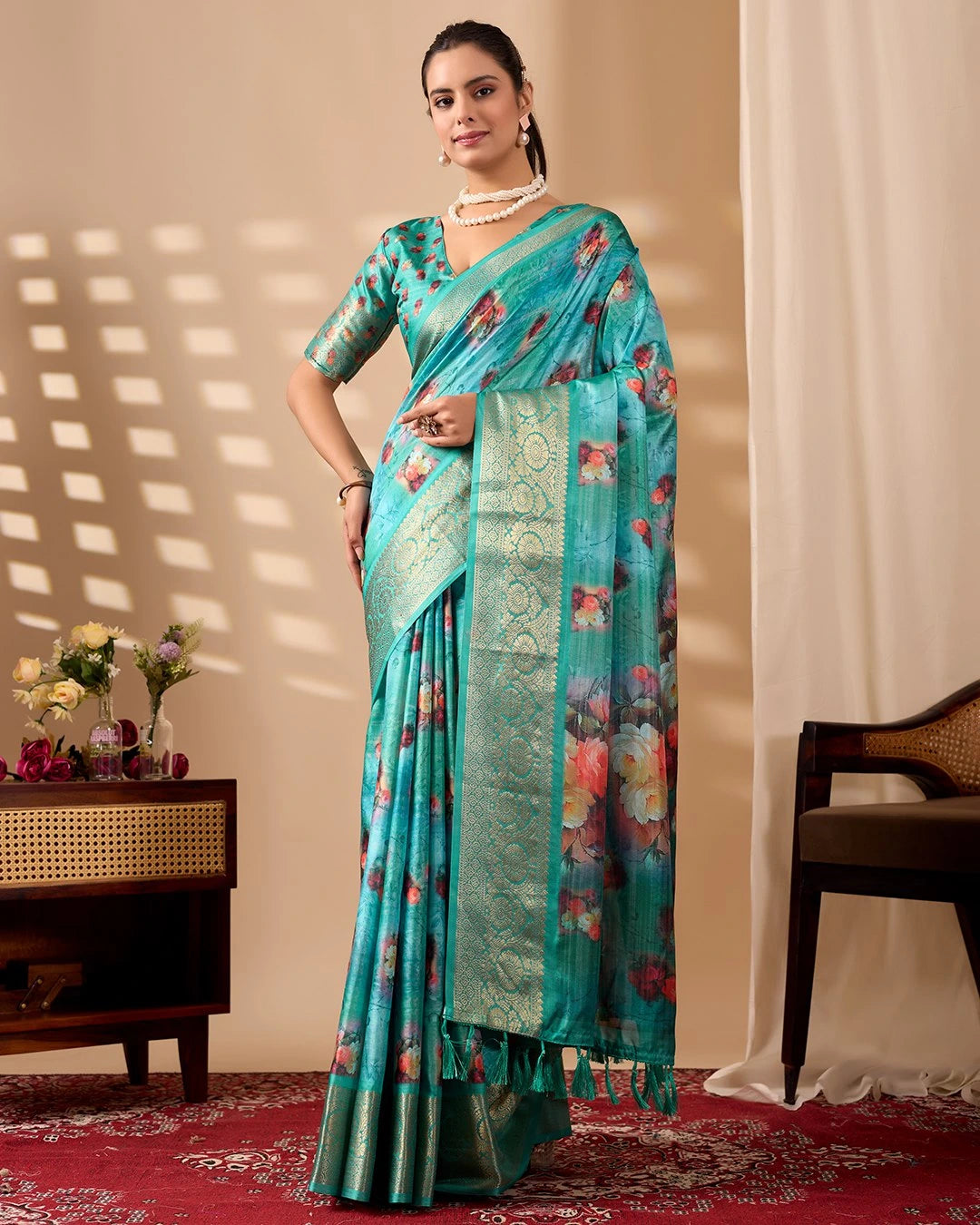 Woman wearing a turquoise saree with floral patterns in a room with a beige wall and red carpet.