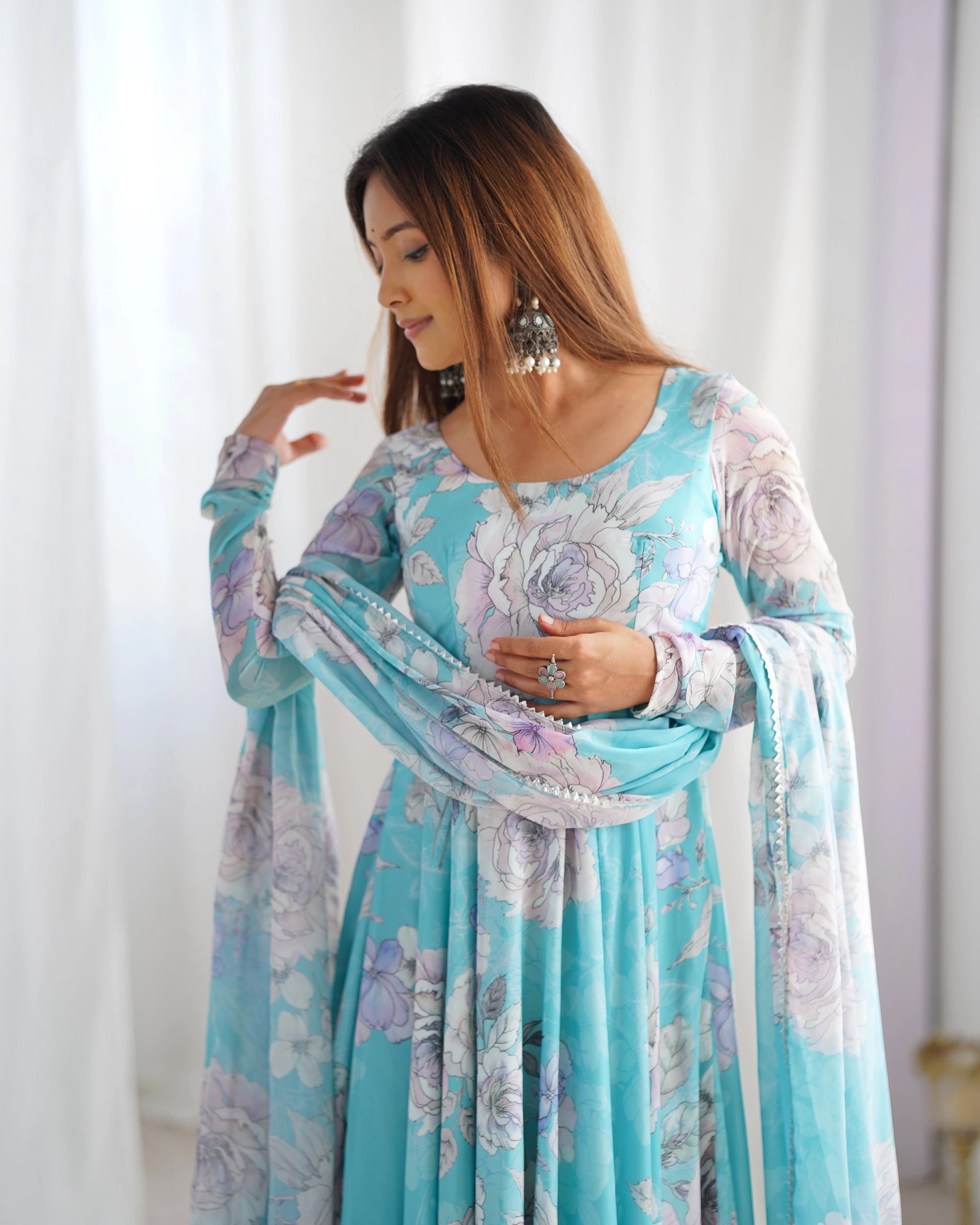 Woman wearing a floral dress with a light blue and white color scheme against a white curtain background.