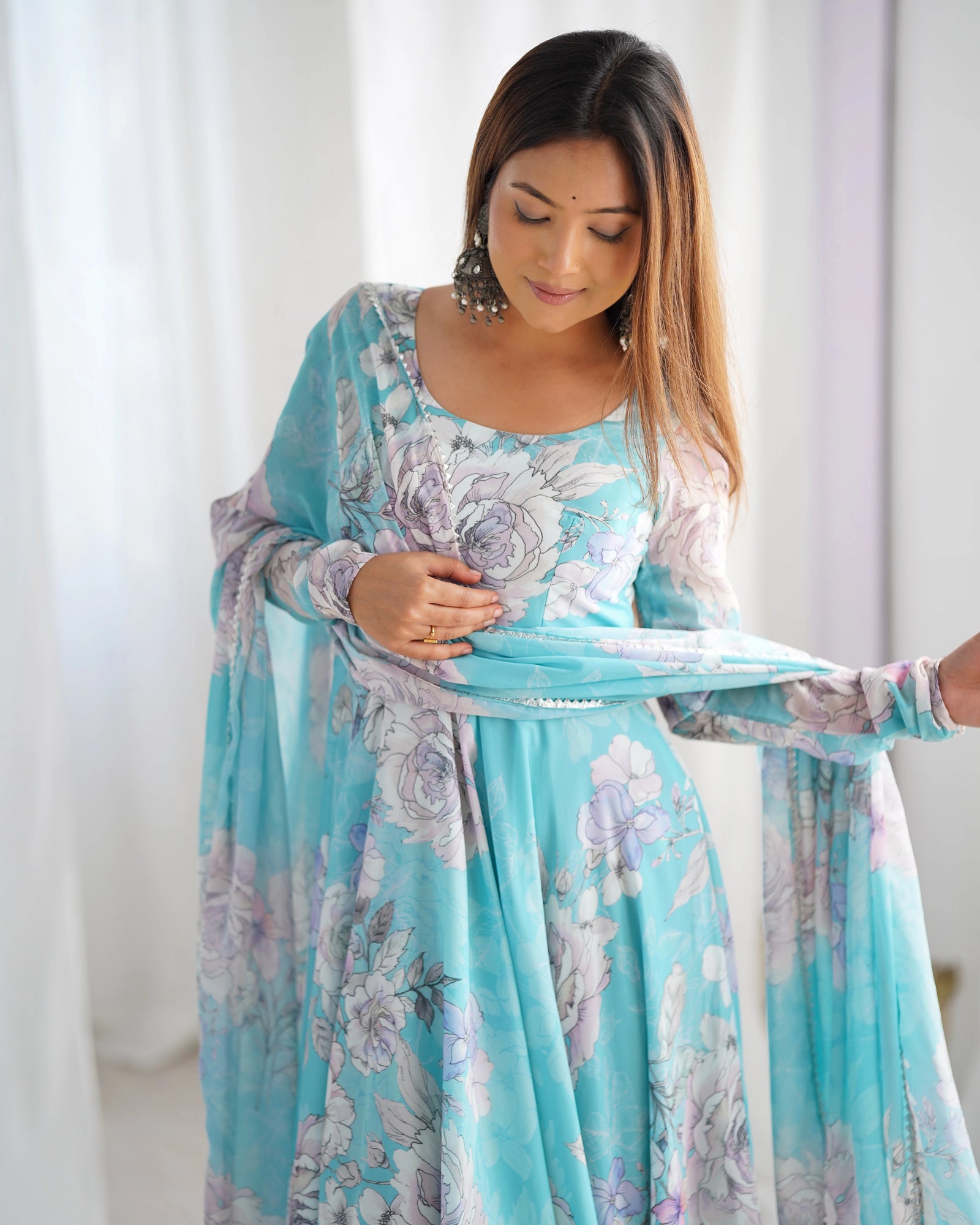 Woman wearing a light blue floral dress with a matching cardigan in a white room.