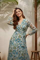 Woman wearing a floral dress standing in a sunlit room with plants.