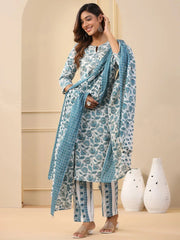 Woman wearing a blue and white patterned outfit with a scarf, standing against a beige wall with decorative vases.
