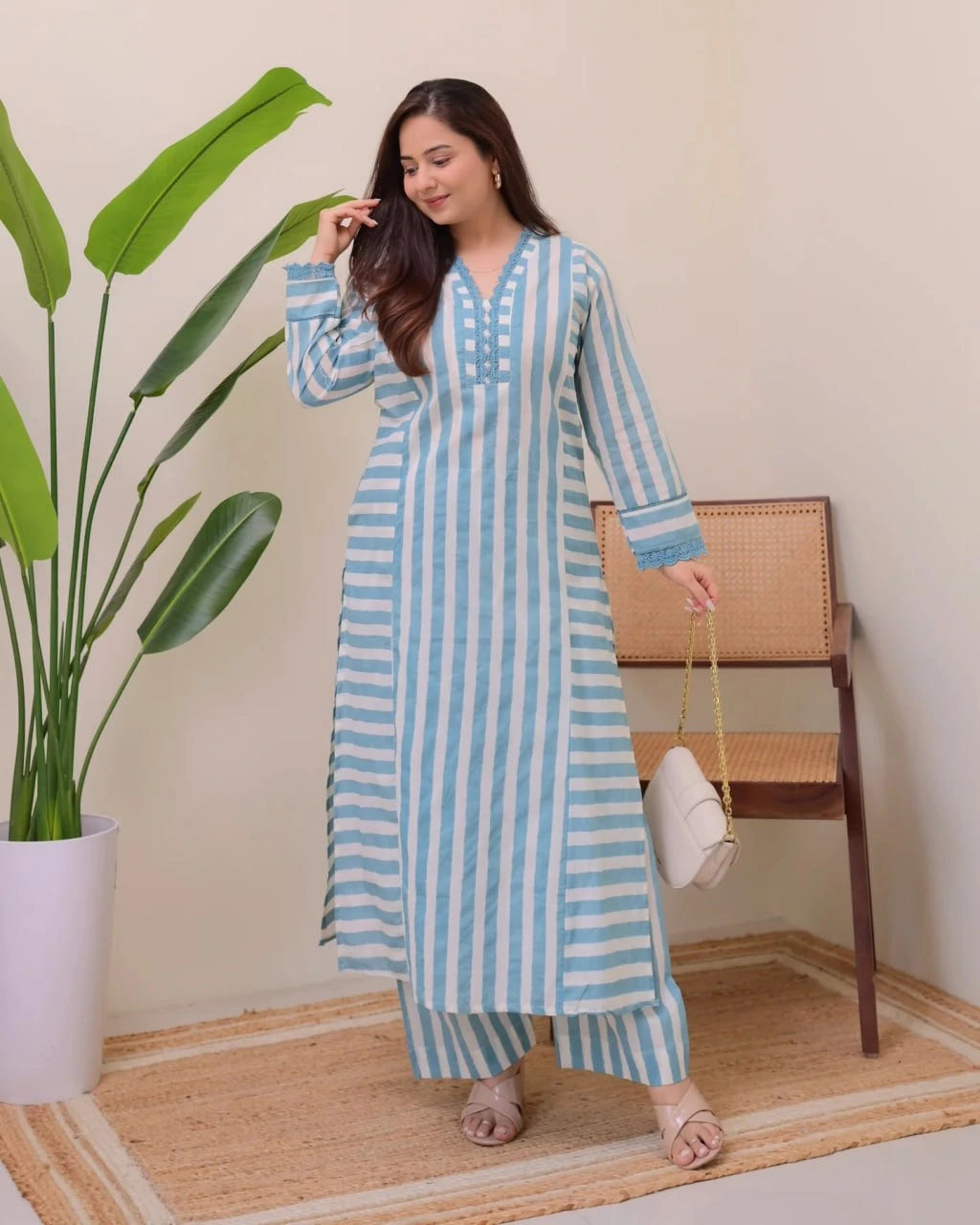 Woman wearing a blue and white striped outfit standing in a room with a plant and chair.