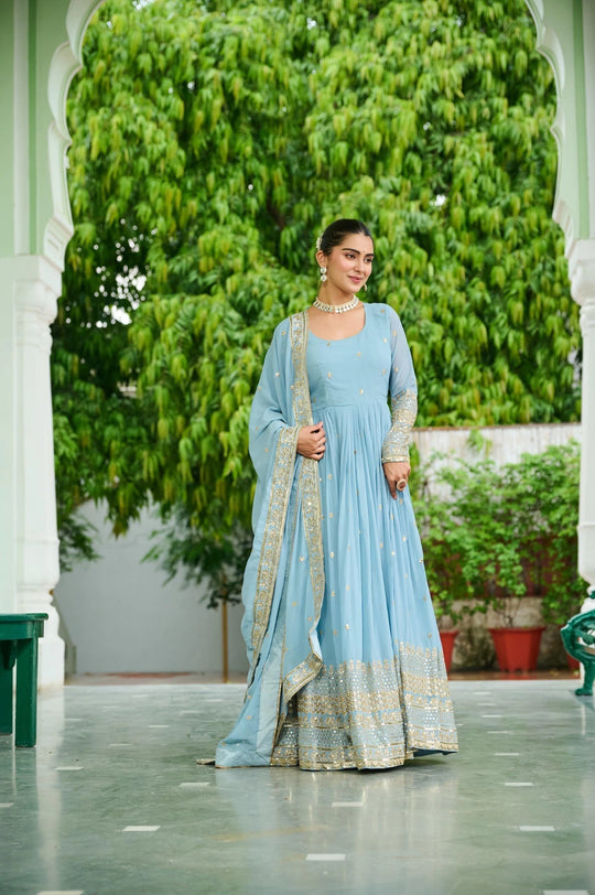 Woman in a light blue traditional outfit standing in a garden setting
