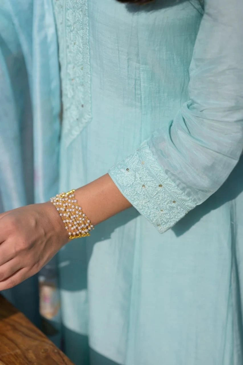 Light blue shirt with rolled-up sleeves and a bracelet worn on a wrist.
