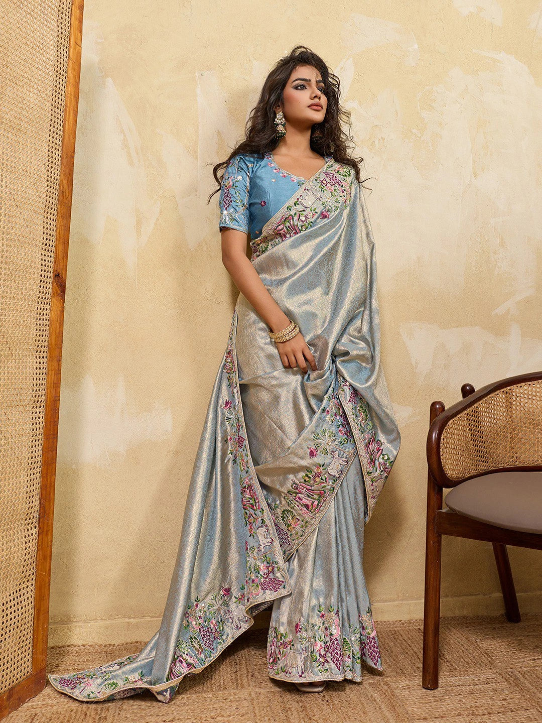 Woman wearing a floral saree with a blue blouse against a beige wall.