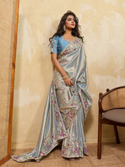 Woman wearing a floral saree with a blue blouse against a beige wall.