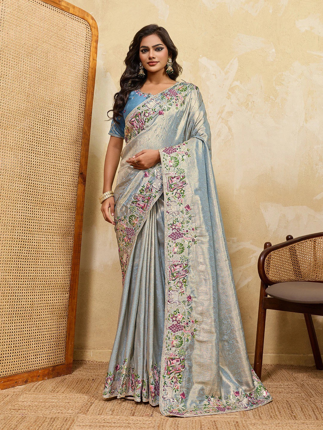 Woman wearing a floral saree with a blue blouse against a beige wall.