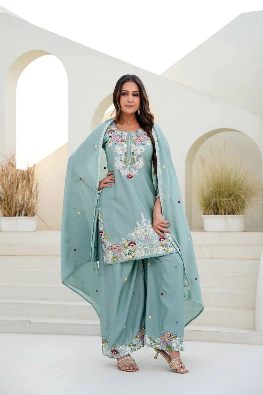 Woman in a light blue embroidered traditional outfit standing in a decorative setting.