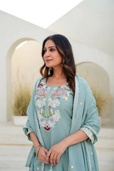 Woman wearing a light blue embroidered outfit in an outdoor setting with arches.