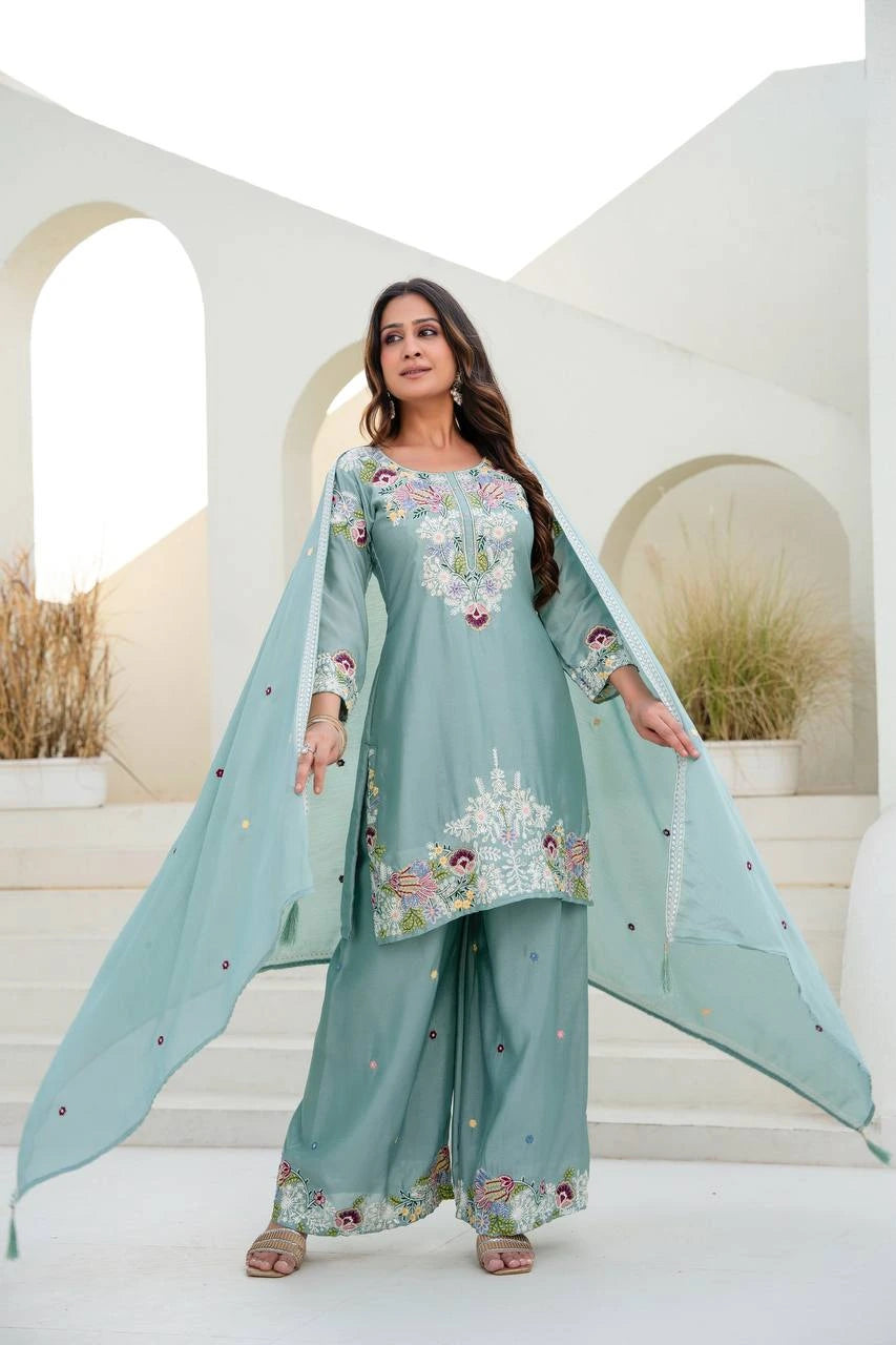 Woman wearing a light blue embroidered traditional outfit in an outdoor setting.