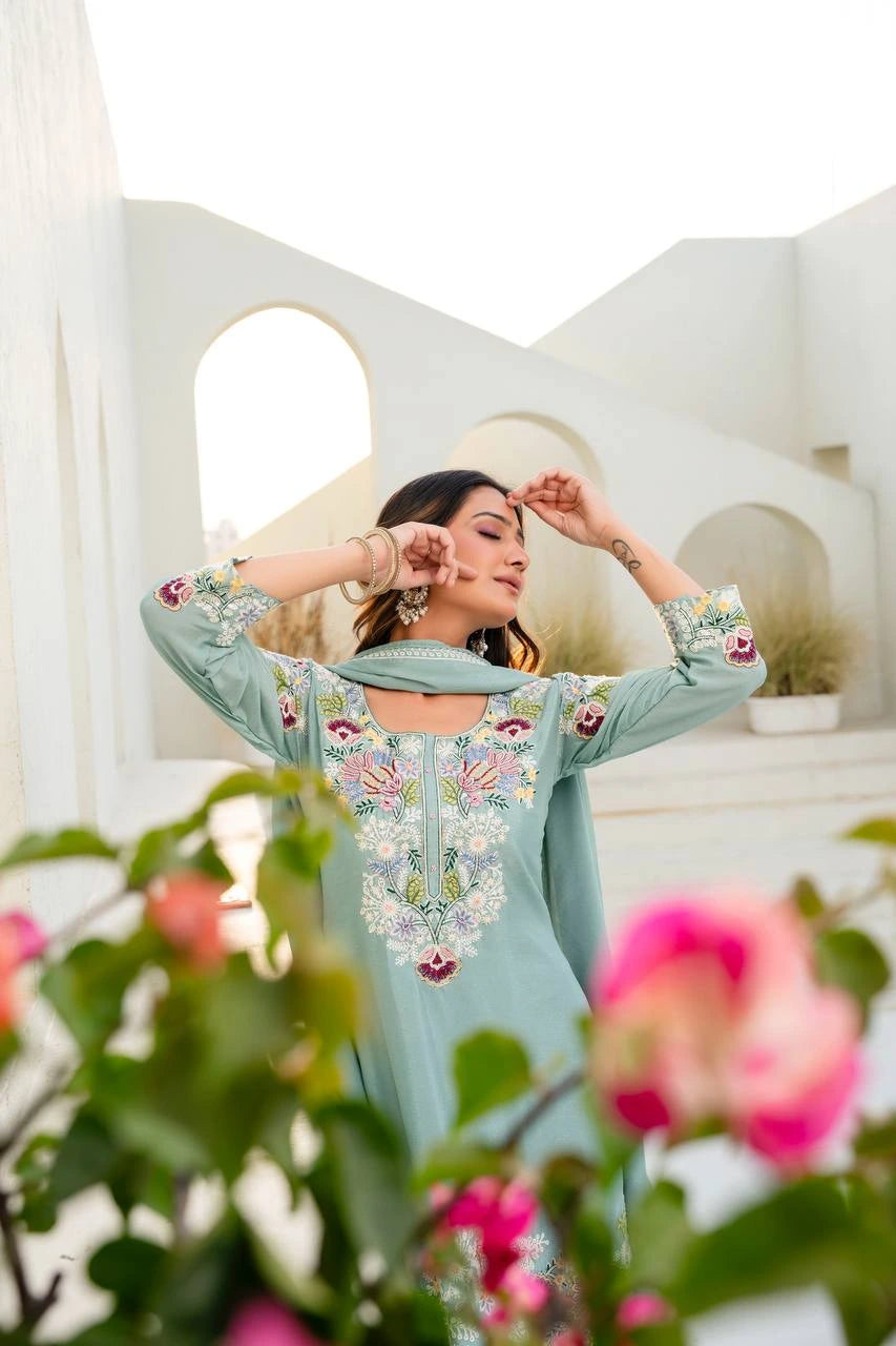 Woman wearing a light blue embroidered dress with pink flowers in an outdoor setting.