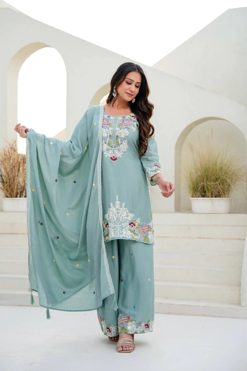 Woman in a light blue embroidered traditional outfit standing in a decorative setting.