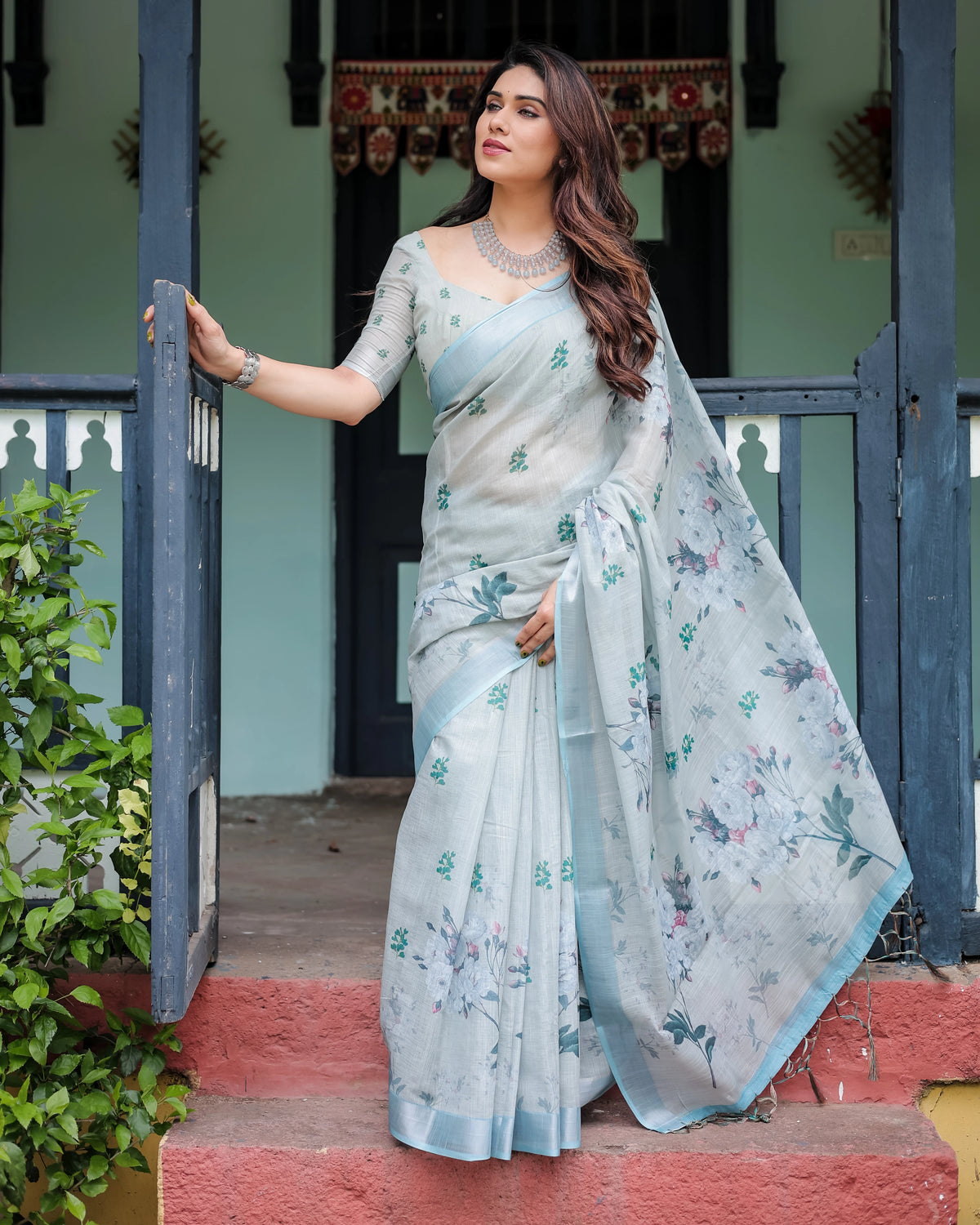 Woman in a light blue saree standing on steps outside a building.
