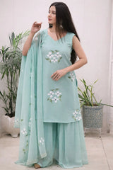 Woman wearing a light blue traditional outfit with floral patterns indoors.