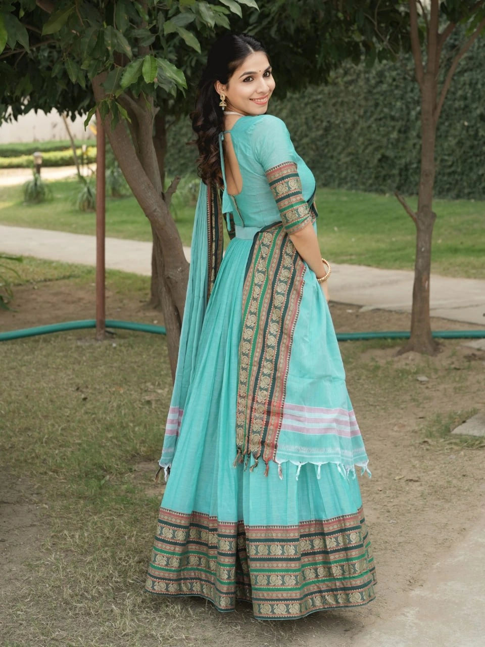 Woman in a light blue traditional outfit with greenery in the background