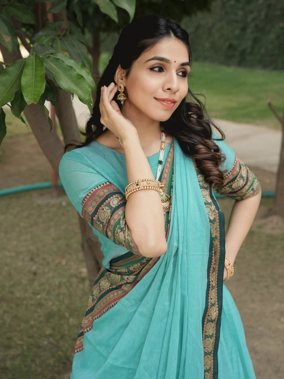 Woman in a teal saree with gold border outdoors