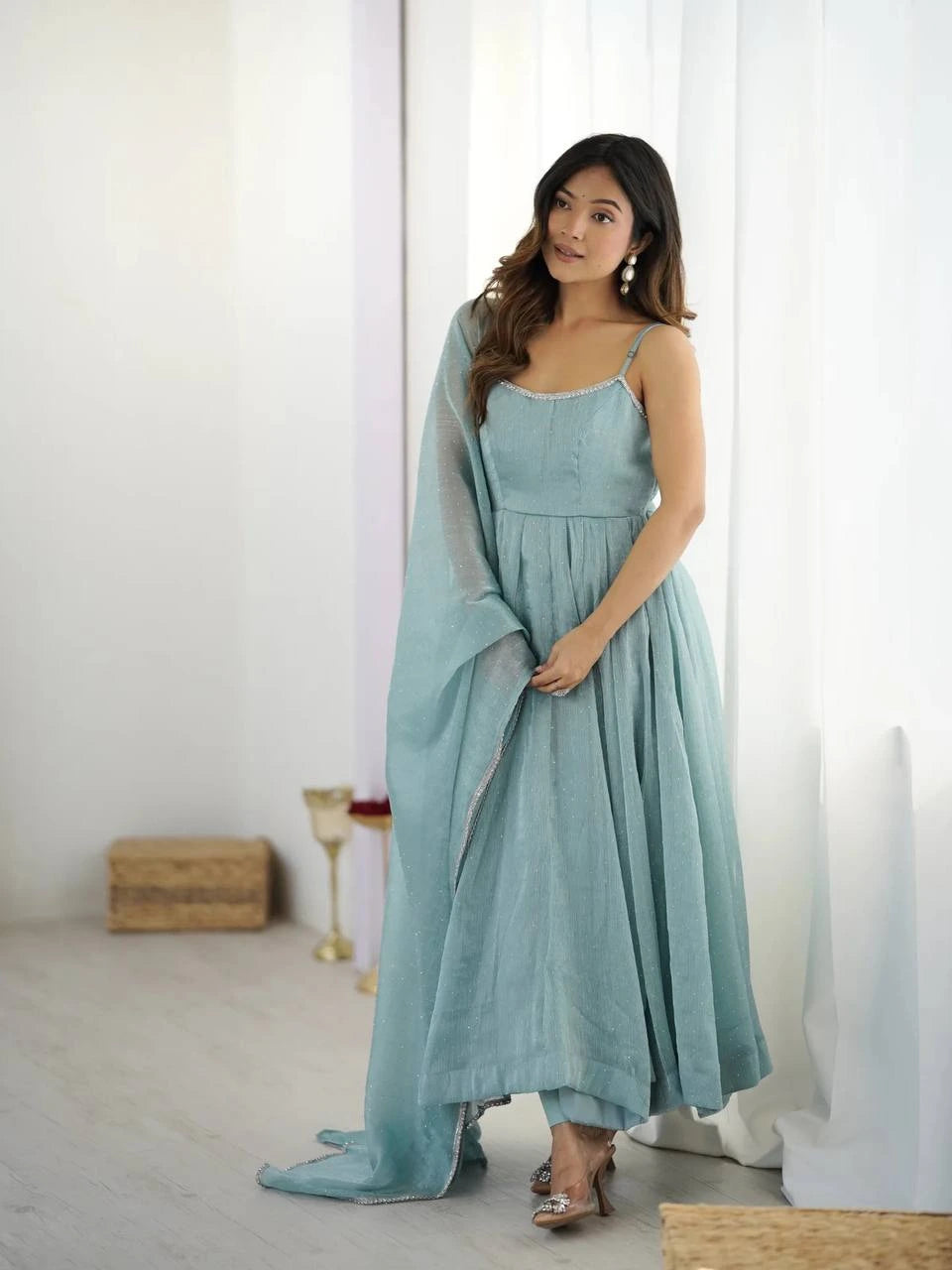 Woman wearing a light blue dress with a matching shawl in a minimalistic room.