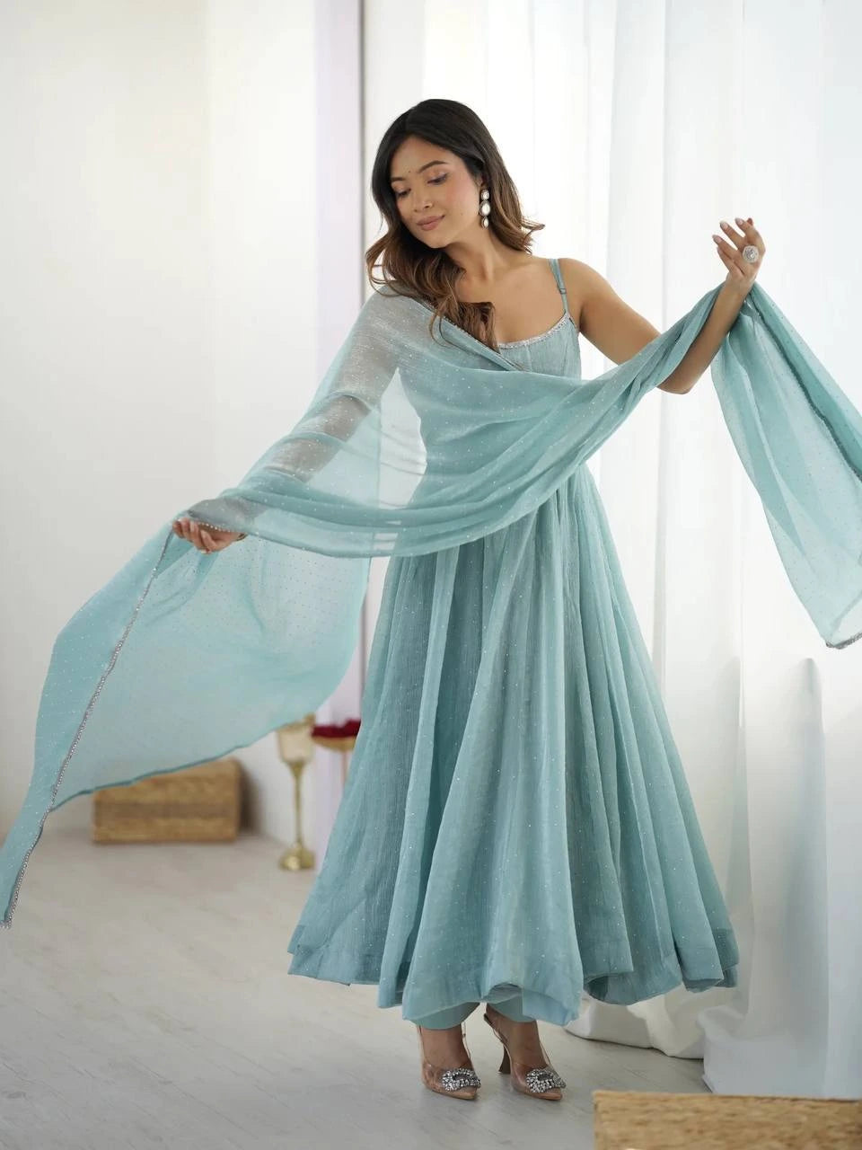 Woman wearing a light blue dress with a sheer overlay in a bright room.