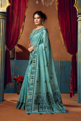 Woman in a teal embroidered dress standing in front of red curtains.