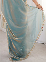 Light blue saree with gold trim being held by a person on a light wooden floor.
