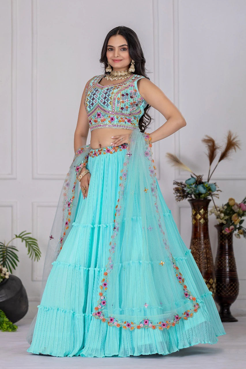 Woman wearing a turquoise embroidered lehenga with a white wall and decorative plants in the background