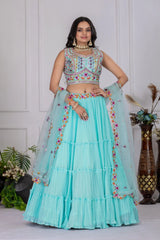 Woman wearing a light blue traditional outfit with intricate designs against a white wall.