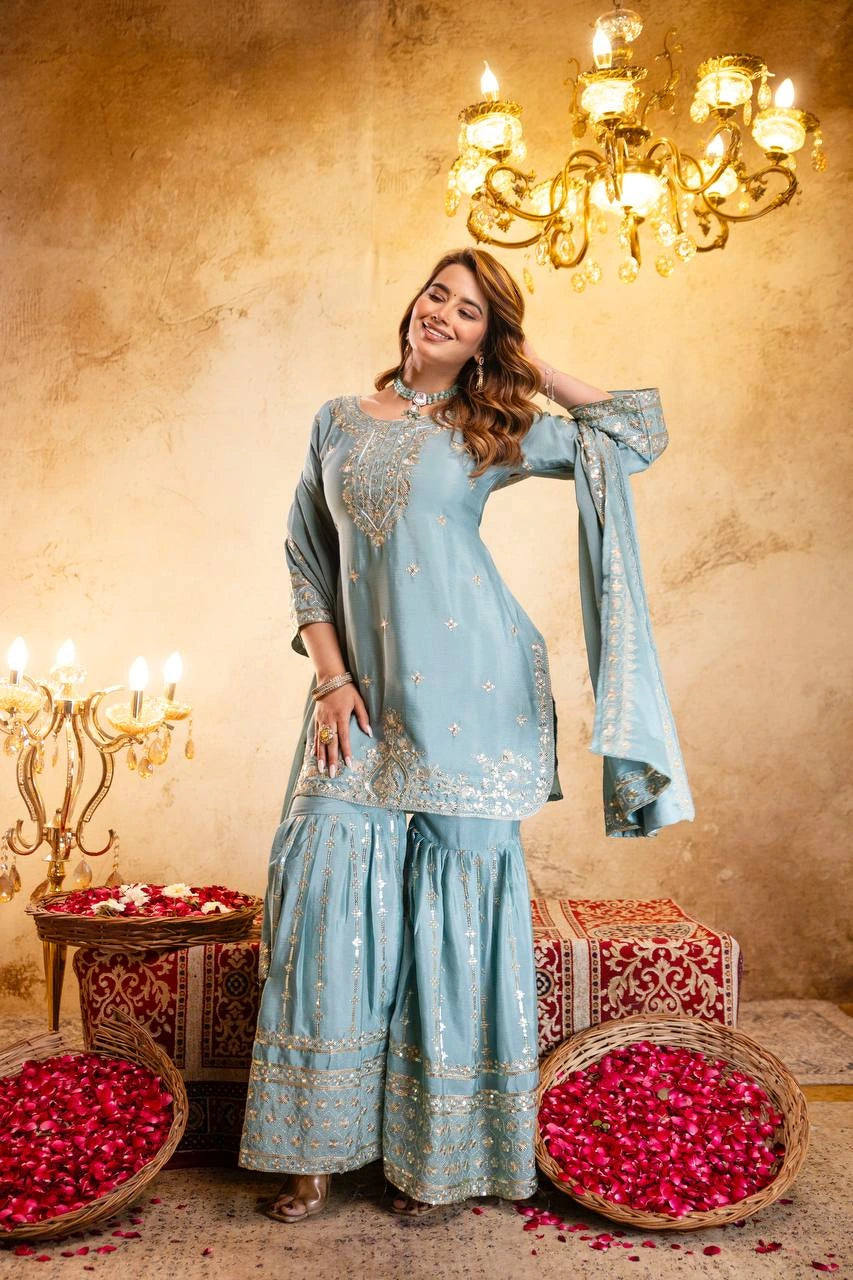 Woman in a light blue traditional outfit standing in a decorated room with chandeliers and rose petals.