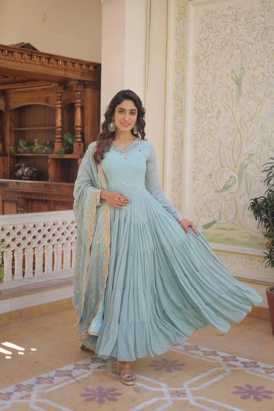 Woman in a light blue traditional outfit standing in an ornate room.