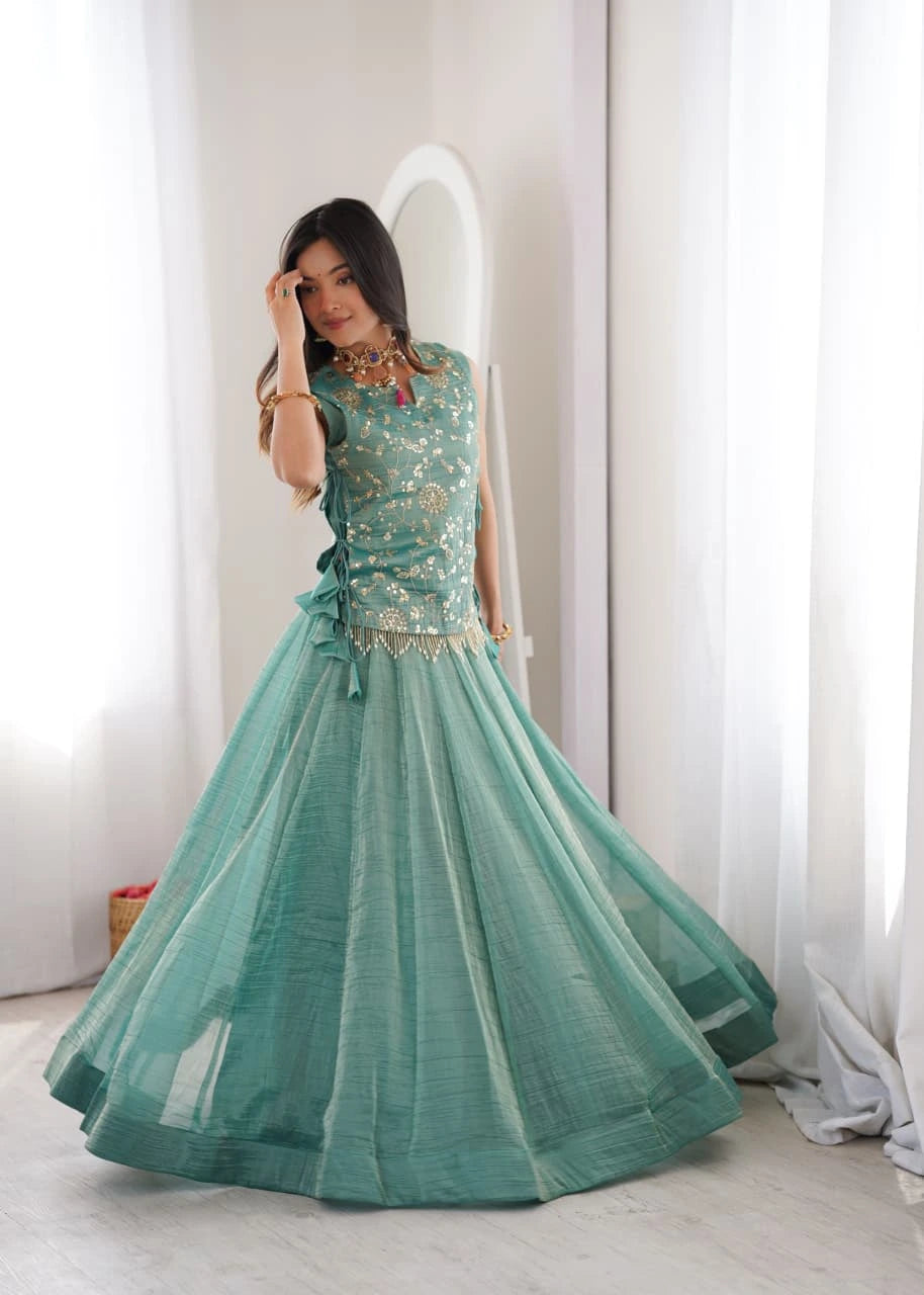 Teal traditional outfit with embroidered top and ruffled dupatta on a stand against a decorative wall.