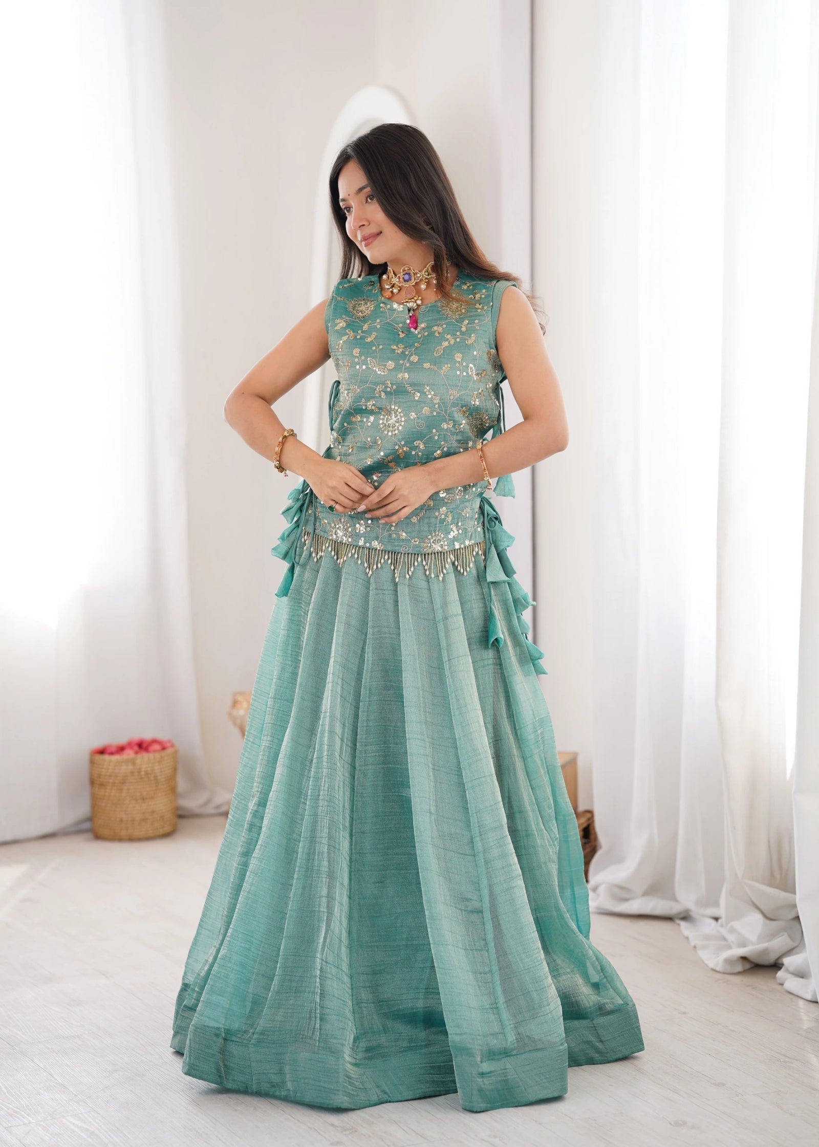 Woman wearing a teal traditional outfit with white curtains in the background