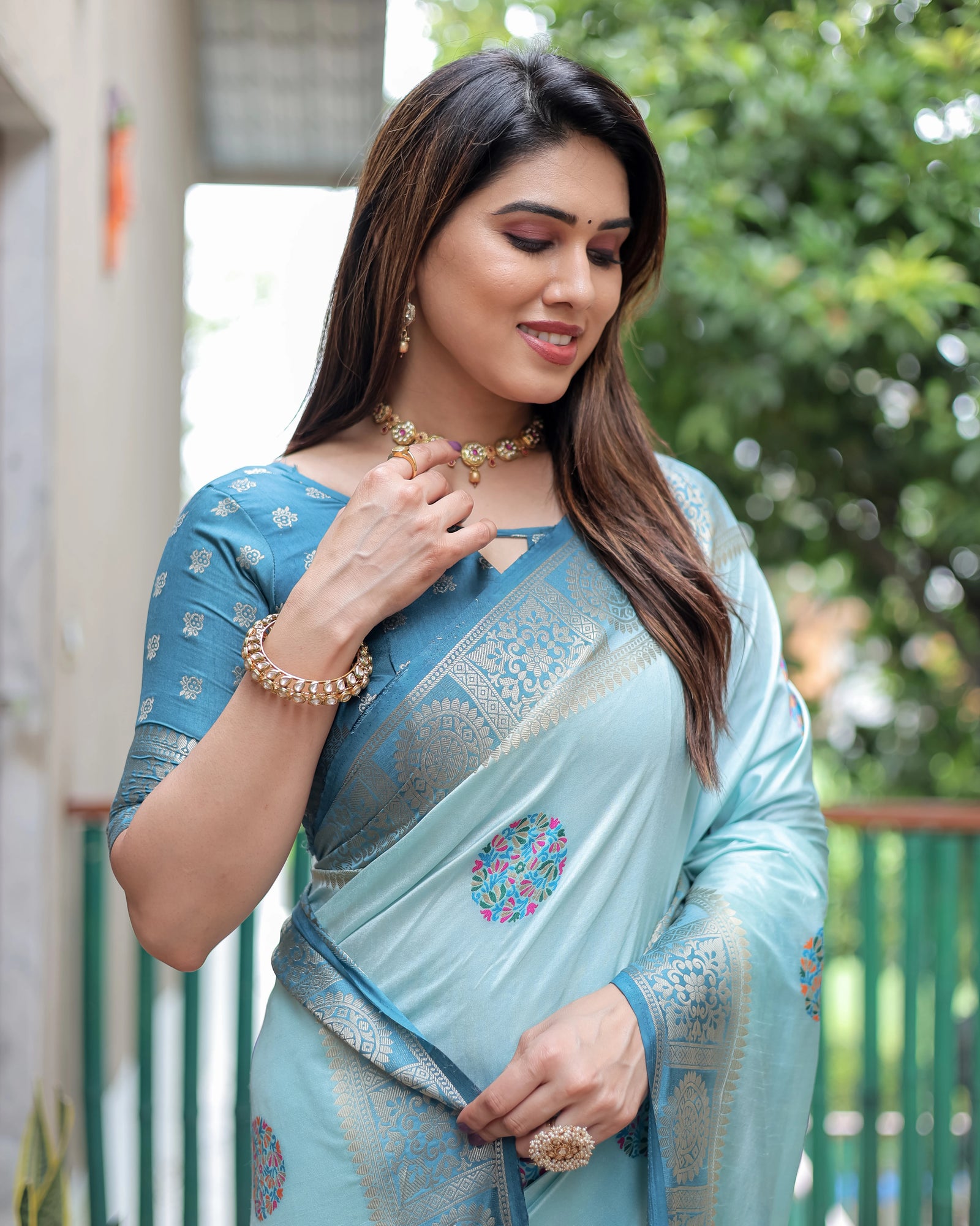Woman wearing a light blue saree with intricate patterns, standing outdoors.
