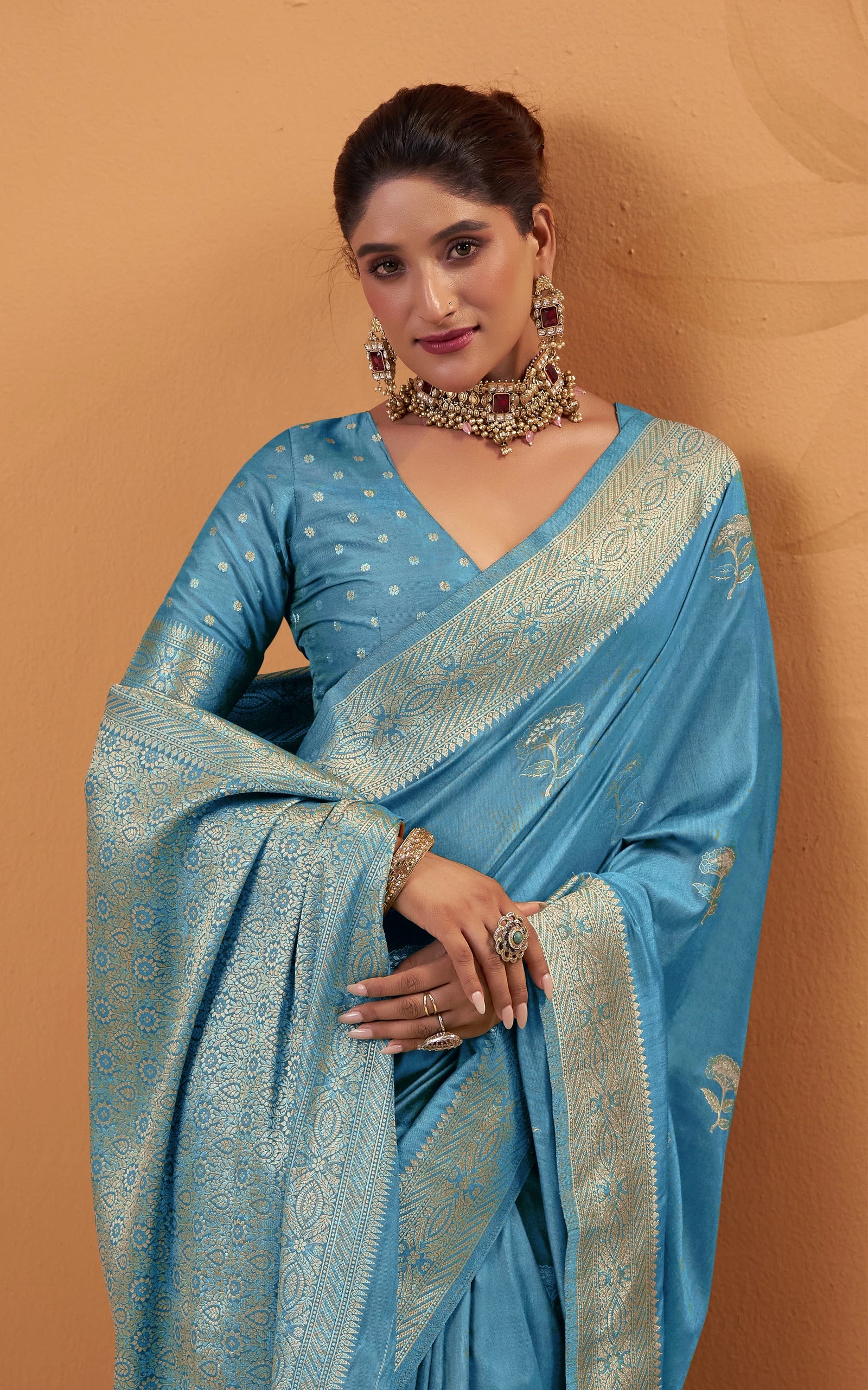 Woman wearing a blue saree with intricate patterns against a beige background