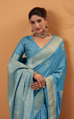 Woman wearing a blue saree with intricate patterns against a beige background