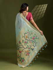 Woman wearing a light blue saree with floral embroidery and tassels on a green background