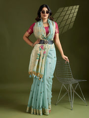 Woman in a light blue saree with a floral blouse standing against a green background