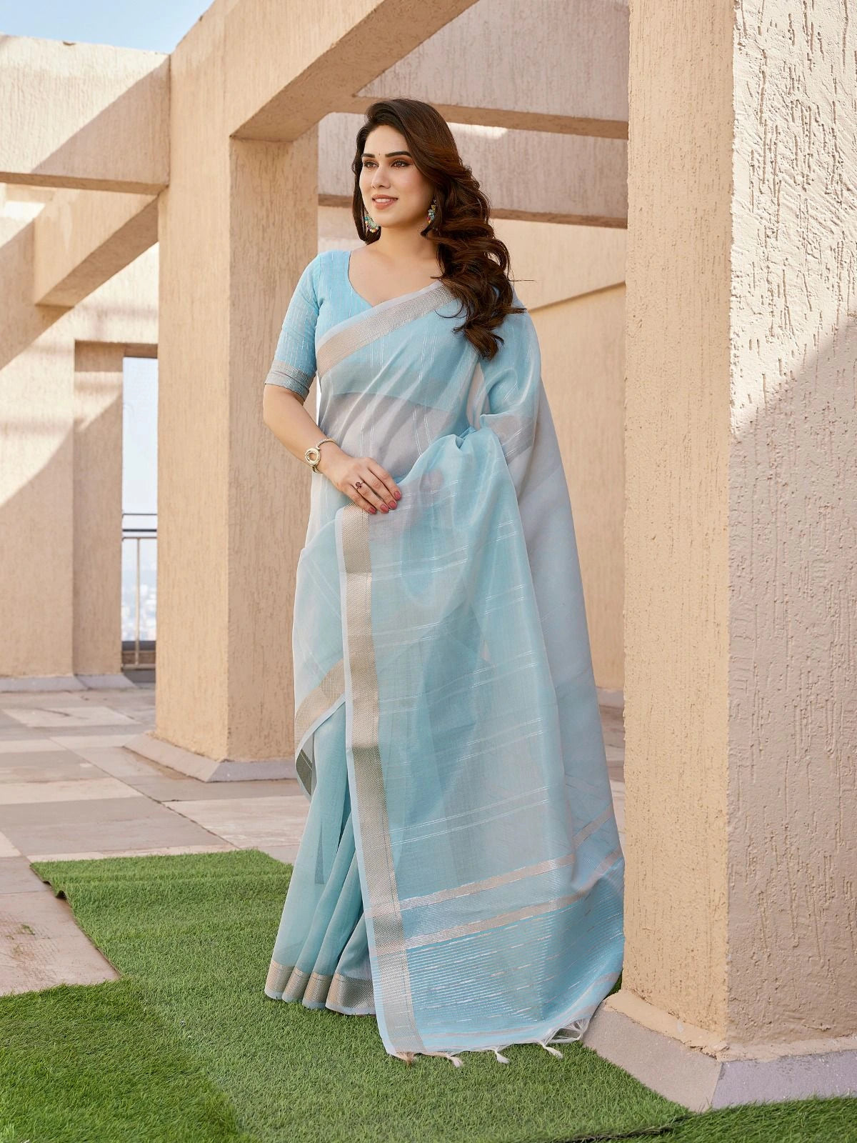 Woman in a light blue saree standing in front of a building with columns.