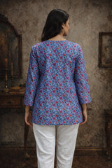 Woman wearing a blue floral blouse and white pants in a rustic setting