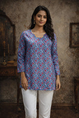 Woman wearing a blue floral top and white pants in a rustic setting