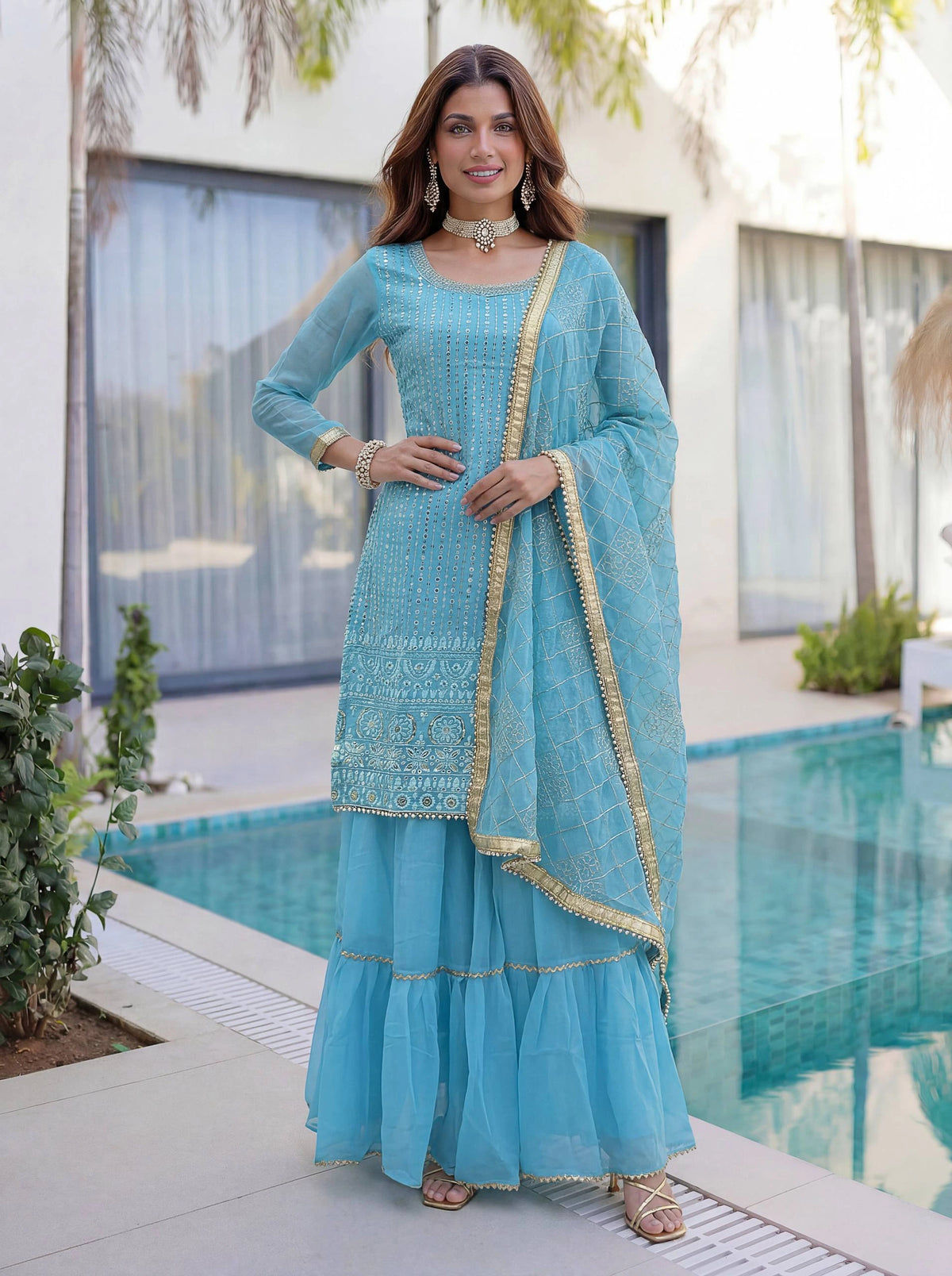 Woman in a light blue traditional outfit standing by a pool.