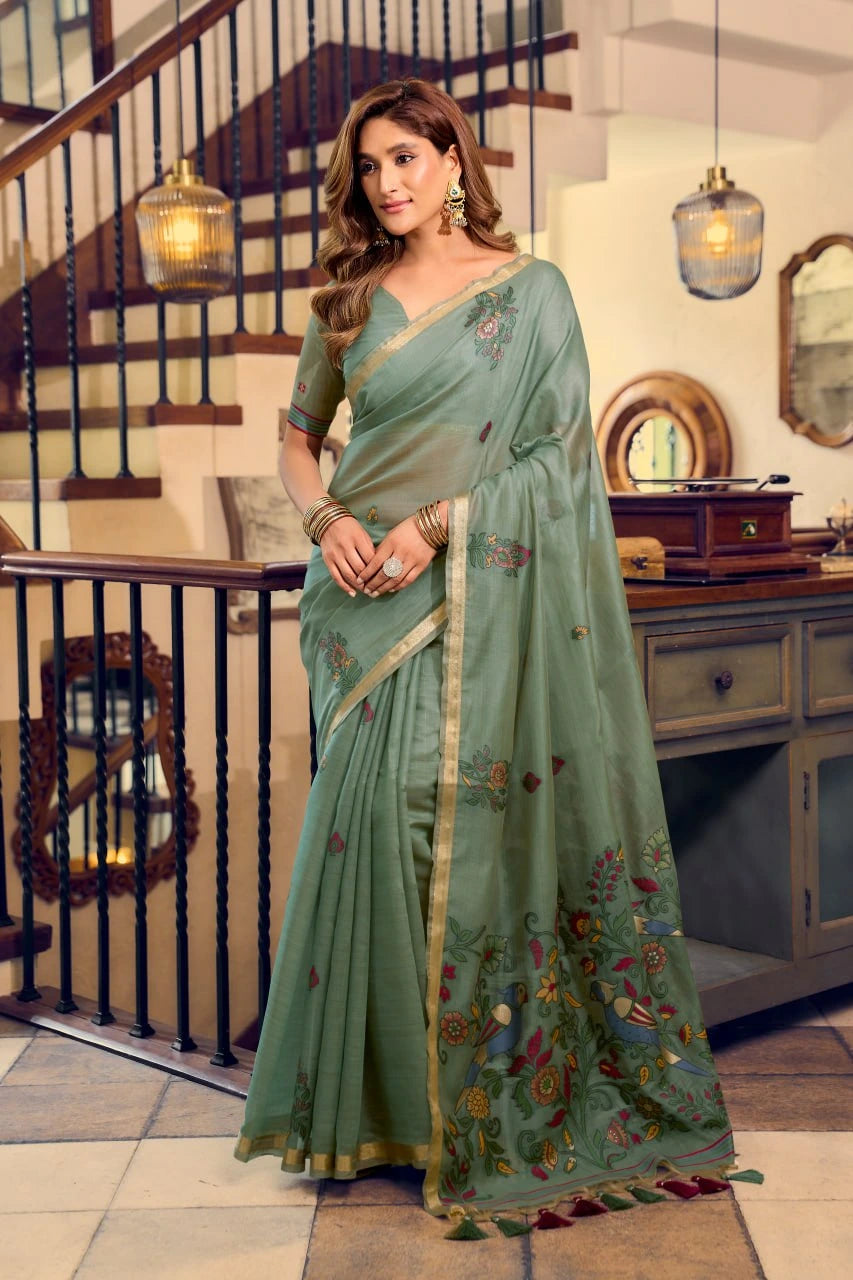 Woman wearing a green saree with floral patterns in an indoor setting.
