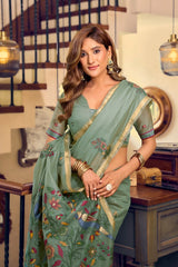 Woman wearing a green saree with floral patterns in an indoor setting.