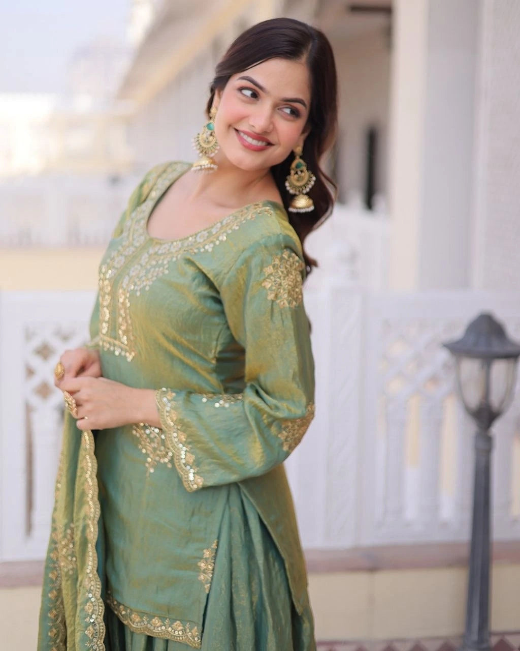 Woman in a green traditional outfit with gold embroidery outdoors.