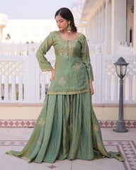 Woman in a green traditional outfit with gold embroidery standing on a patio.
