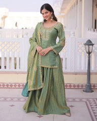 Woman in a green traditional outfit with gold embroidery standing in a decorative indoor setting.