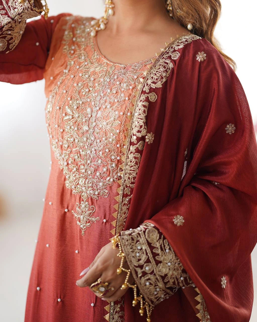 Close-up of a traditional embroidered outfit with gold detailing on a plain background